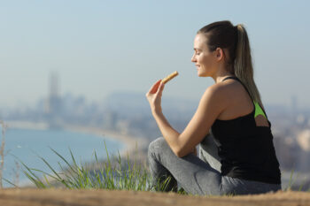 Jogger eating energy bar after sport sitting outdoors in a city outskirts